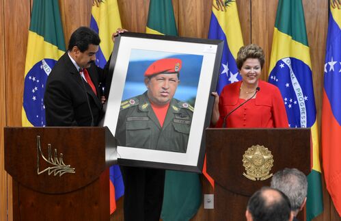 Er ist der neue starke man an der Spitze Venezuelas - oder sollte es jedenfalls sein: Nicolas Maduro. Der Politiker, hier links im Bild mit der brasilianischen Präsidentin Dilma Rousseff, der Vereinigten Sozialistischen Partei war bereits Außenminister und Vizepräsident, bis er nach dem Tod seines erkrankten Vorgängers Hugo Chávez 2013 selbst zum Staatspräsidenten gewählt wurde. Dennoch steht Chávez, der kaum übersehbar auf dem Gastgeschenk prangt, weiterhin als venezolanische Ikone unübersehbar für das Land. Seit 1999 leitete er die Geschicke des Landes nach dem Vorbild Simón Bolívars und dessen Einsatz für ein vereintes Südamerika. Person, Politik, Führungsstil und Medienauftritte waren stets umstritten, riefen aber die Anerkennung in der globalen Linken aufs Parkett. Insbesondere sein autoritäres Vorgehen und seine schwache Entwicklungspolitik wurden im vorgehalten.
