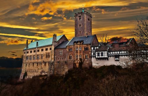 Am 31. Oktober 1517 soll Martin Luther Überlieferungen zufolge seine Reformationsthesen an die Wittenberger Schlosskirche geschlagen haben – ein Erdbeben für die konservative Kirche, gegen deren dubiosen Handel mit Ablassbriefen Luther sich stemmte. Nach einem öffentlichen Spießrutenlauf wird Luther 1521 schließlich „vogelfrei“ gesprochen – jeder kann den Reformator nun ermorden, ohne dafür belangt zu werden. Im Mai 1521 lässt Kurfürst Friedrich der Weise Luther auf die Wartburg bei Eisenach bringen. Der mächtige Fürst hofft, Luther kurzzeitig aus dem Rampenlicht zu nehmen und die ständigen Angriffe auf die reformatorische Bewegung abzuschwächen. Dort verbringt Luther unfreiwillig ein knappes Jahr. Inkognito unter dem Decknamen Junker Jörg übersetzte er das Neue Testament in ein allgemein verständliches Deutsch. In der weltbekannten Lutherstube an einem Kastentisch leistet er hier nicht nur einen bedeutenden Beitrag für die Theologie, sondern auch für die Vereinheitlichung der Landessprache. Der originale Tisch, an dem Luther das Neue Testament übersetzte, soll später Splitter für Splitter in den Taschen der Pilger verschwunden sein, bis er in sich zusammenfiel – sogar Zahnschmerzen sollte es heilen, wenn man sich so einen Span dann in den Mund steckte.