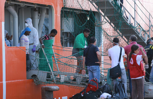 Sie haben es geschafft – Helfer erwarten ein Rettungspost voller Flüchtlinge zur Anlandung in Catania, Sizilien, im Juli 2015 auf einem Schiff der Operationo Triton. Schlepper schicken oft viele Boote gleichzeitig aufs Meer. Das macht es für die Retter der internationalen Flotte schwer, rechtzeitig zur Stelle zu sein, um den Flüchtlingen helfen zu können. Einer von 29 stirbt. Nie zuvor war es so gefährlich für Flüchtlinge, das Mittelmeer zu überwinden.
