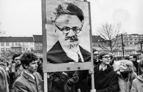 In den 1960er-Jahren gingen immer mehr Studenten weltweit auf die Straße – auch in Deutschland. Sie waren meist linksgerichtet, gesellschaftskritisch und politisch eingestellt – und strebten eine umfassende Demokratisierung der bundesdeutschen Gesellschaft als Beitrag zur Emanzipation aller Menschen von Ausbeutung und Unterdrückung an. Hier demonstrieren zwei junge Männer mit einem Transparent, das Leo Trotzki zeigt. Der russische Revolutionär, kommunistische Politiker und marxistische Theoretiker war der maßgebliche Organisator der Revolution vom 25. Oktober und 7. November 1917, der die Bolschewiki unter der Führung von Wladimir Iljitsch Lenin an die Macht brachte. 